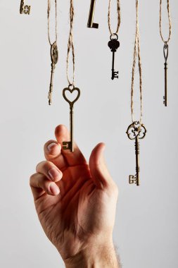 cropped view of man touching vintage keys hanging on ropes isolated on white clipart