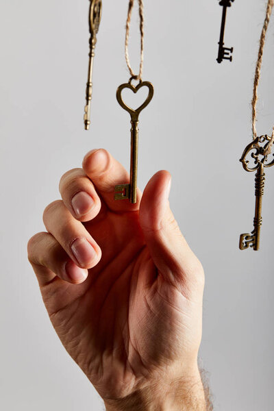 cropped view of man touching vintage keys hanging on ropes isolated on white