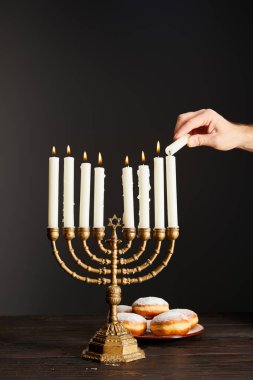 Menorah 'ta mum yakan bir adamın görüntüsü. Hanuka' daki siyah arka planda donutların yanında.
