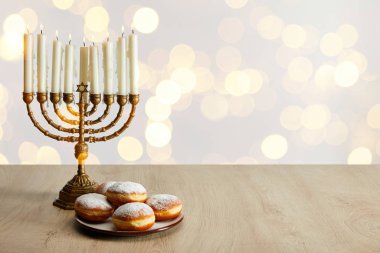 delicious doughnuts near candles in menorah on white background with bokeh lights on Hanukkah clipart