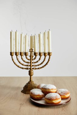 delicious doughnuts near burning candles in menorah on Hanukkah isolated on white clipart
