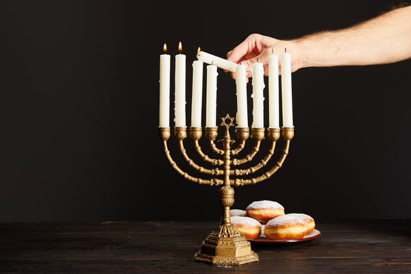 cropped view of man lighting up candles in menorah near doughnuts isolated on black