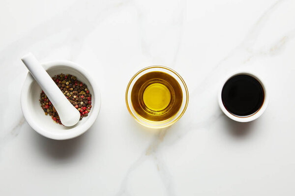 Top view of olive oil, soy sauce and peppercorns in bowls on marble background