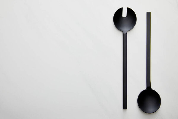 Top view of black ladle and spoon on marble background