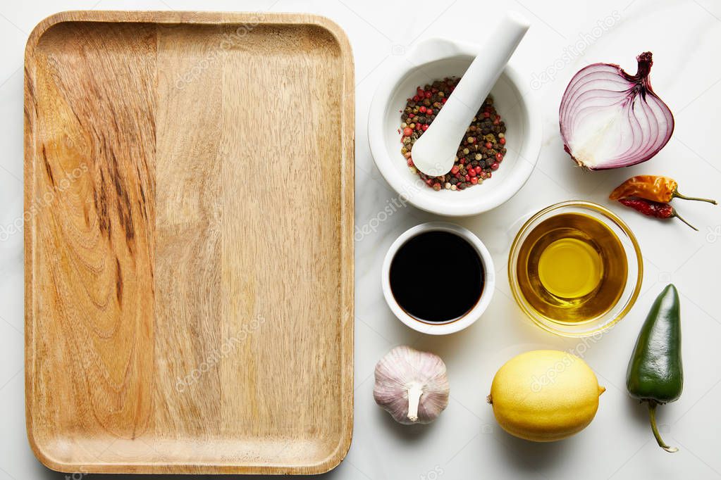 Top view of soy sauce, olive oil with spices and lemon beside wooden plate on marble background