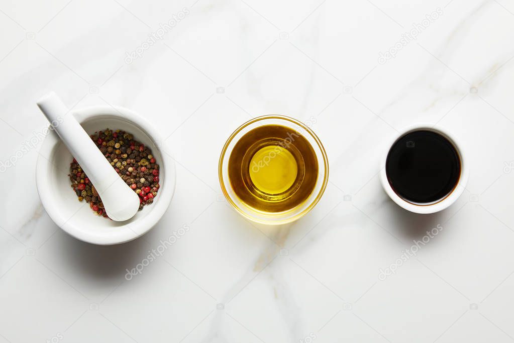 Top view of olive oil, soy sauce and peppercorns in bowls on marble background
