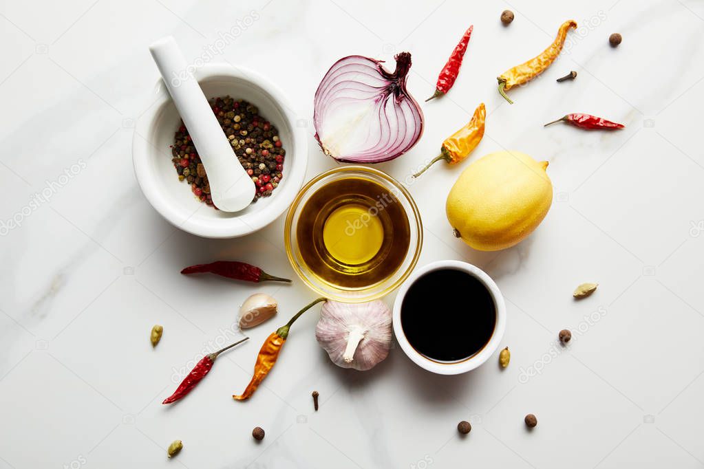 Top view of lemon, olive oil with soy sauce and spices on marble background