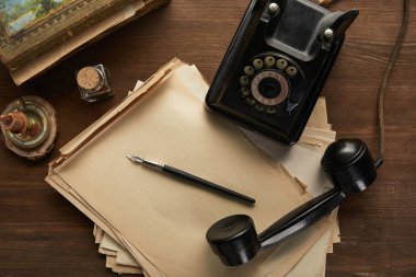 top view of vintage paper, painting, fountain pen, candle and dial phone on wooden table clipart