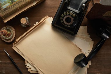 Eski kağıt, resim, dolmakalem, mum ve ahşap masadaki çevirmeli telefonun üst görüntüsü