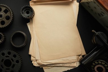 Siyah yüzey üzerinde eski viteslerin ve vintage saatin yanındaki boş kağıtların üst görünümü