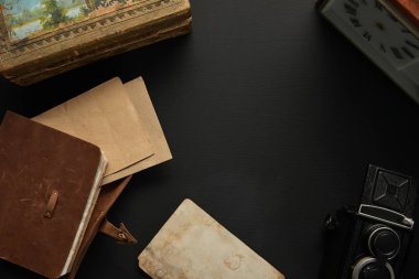 Siyah arkaplanda eski kamera, kağıt, resim, saat ve not defterinin üst görünümü