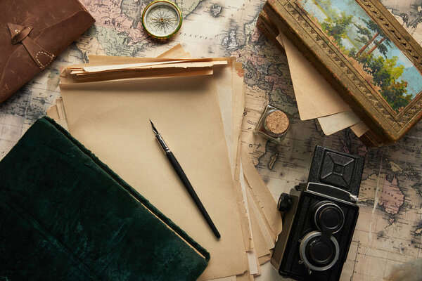 top view of vintage camera, compass, fountain pen, photo album, paper and painting on map background