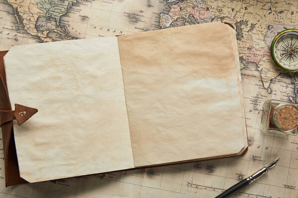 top view of vintage blank notebook with fountain pen near compass on map background