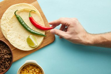 Elinde tortilla, kıyma ve mavi arka planda tortilla olan kırmızı biber tutan adamın en iyi görüntüsü.
