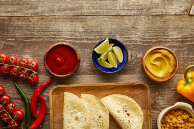 Olgun sebzeler, tortillalar ve ahşap arka planda soslar.