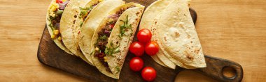 Top view of tasty tacos with cherry tomatoes on cutting board on wooden surface, panoramic shot clipart