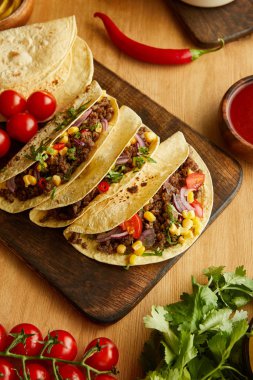 Top view of tacos on cutting board with ripe vegetables on wooden table clipart