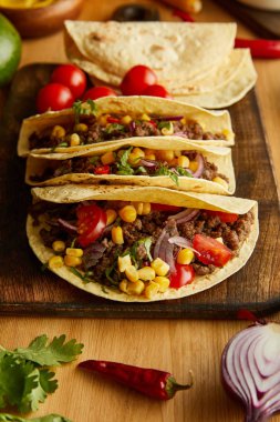 Tacos with minced meat on cutting board with parsley and vegetables on wooden table clipart