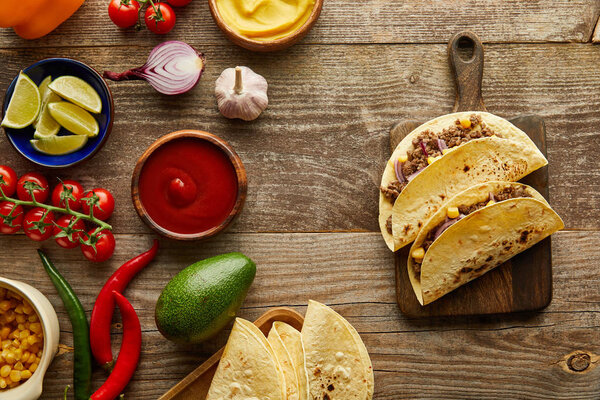 Top view of tacos on cutting board with fresh ingredients on wooden background
