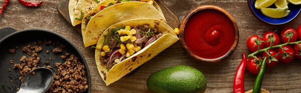 Top view of traditional mexican tacos with ketchup and ingredients on wooden surface, panoramic shot