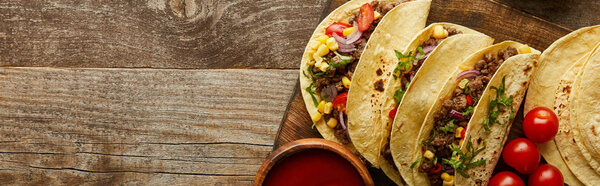 Top view of traditional mexican tacos with cherry tomatoes and ketchup on wooden surface, panoramic shot