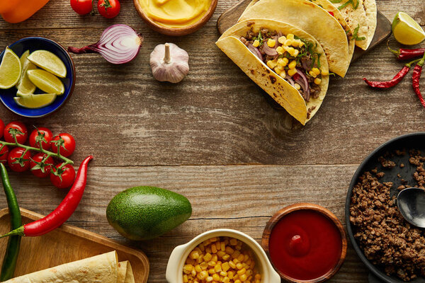 Top view of tacos with fresh ingredients and sauces on wooden background