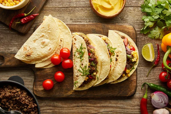 Vista Superior Tacos Saborosos Placa Corte Com Ingredientes Fundo Madeira — Fotografia de Stock