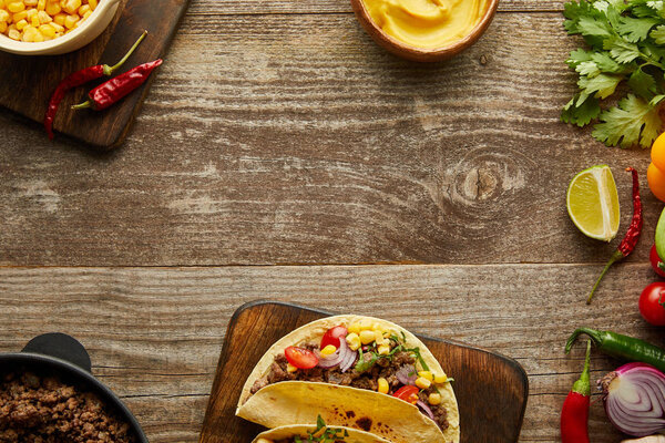Top view of delicious tacos with ingredients and mustard on wooden background
