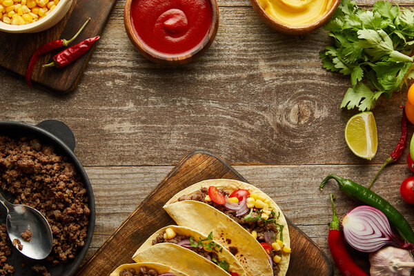 Top view of tasty tacos with minced meat and fresh ingredients on wooden surface