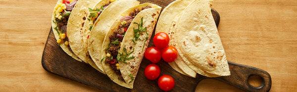 Top view of tasty tacos with cherry tomatoes on cutting board on wooden surface, panoramic shot