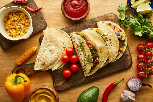 Top view of tacos with meat and fresh ingredients on wooden table