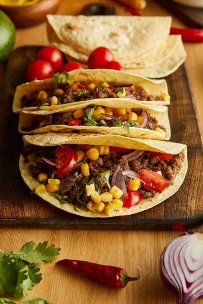 Tacos with minced meat on cutting board with parsley and vegetables on wooden table