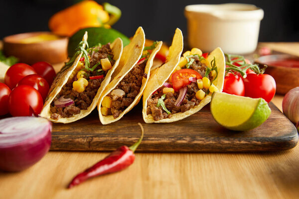 Selective focus of fresh tacos with ingredients on wooden table on black background