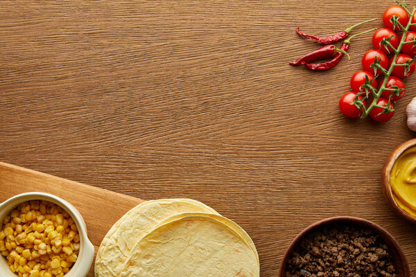 Top view of fresh tortillas with minced meat and vegetables on wooden background