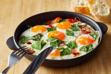 Maydanozlu sahanda yumurta ve ahşap masada kırmızı biber, çatal bıçak ve ekmek.