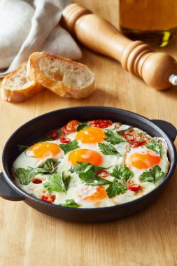 Maydanozlu sahanda yumurta ve ahşap masada biber ve ekmek.
