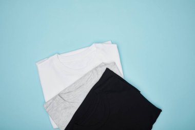 Mavi üzerine izole edilmiş boş siyah, beyaz ve gri tişörtlerin üst görünümü