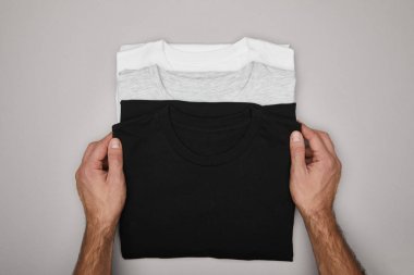 cropped view of man touching blank basic black, white and grey t-shirts isolated on grey clipart