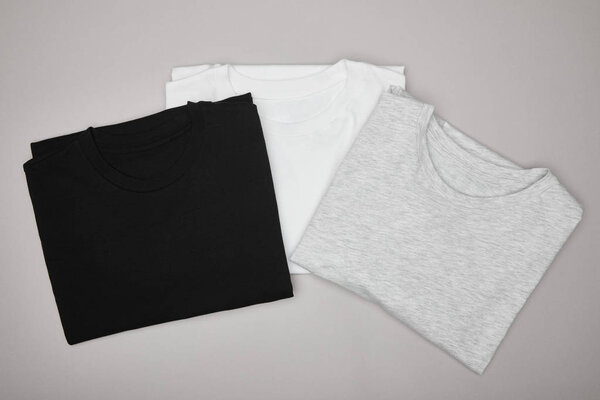 top view of blank basic black, white and grey t-shirts isolated on grey