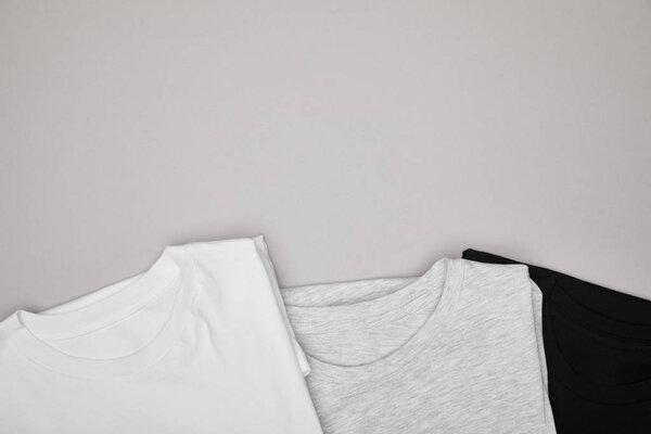 top view of blank basic black, white and grey t-shirts isolated on grey