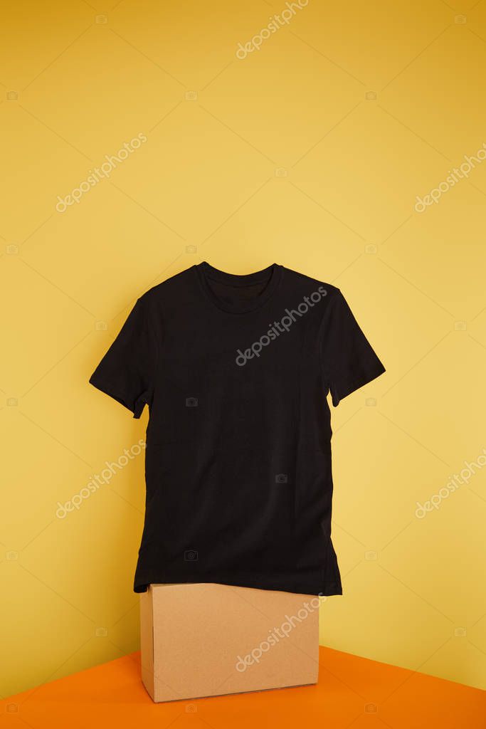 Basic black t-shirt on cube on yellow background