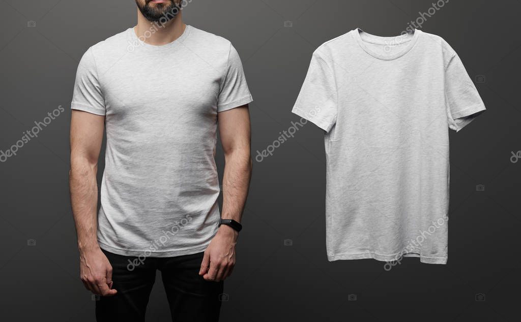 Cropped view of bearded man near blank basic grey t-shirt on black background