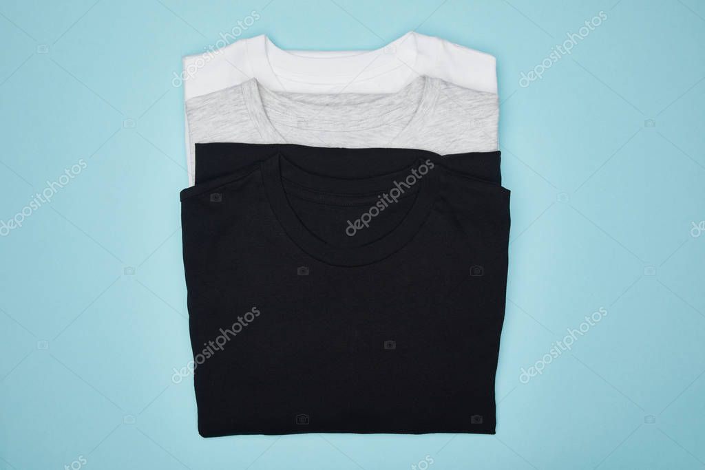 Top view of blank basic black, white and grey t-shirts isolated on blue