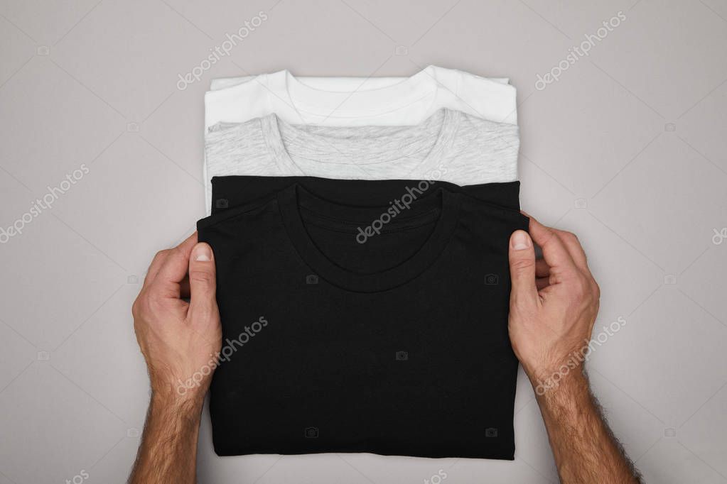Cropped view of man touching blank basic black, white and grey t-shirts isolated on grey
