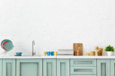 modern white and turquoise kitchen interior with kitchenware near brick wall clipart