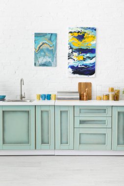 Modern beyaz ve turkuaz mutfak iç dekorasyonu mutfak malzemeleri ve tuğla duvarda soyut resimler.