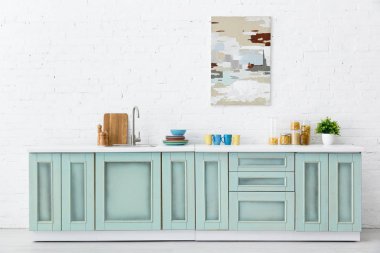 Beyaz ve turkuaz mutfak iç dekorasyonu mutfak gereçleri ve tuğla duvarda soyut resim