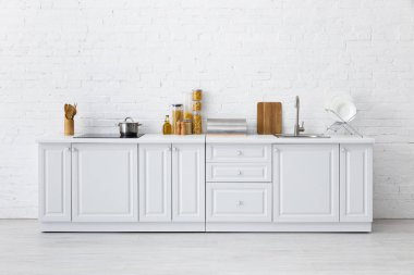 Minimalist modern beyaz mutfak. Tuğla duvarın yanında mutfak gereçleri var.