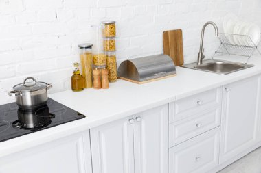 minimalistic modern white kitchen interior with kitchenware near brick wall clipart