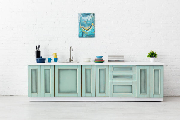 white and turquoise kitchen interior with sink, tableware and abstract painting on brick wall